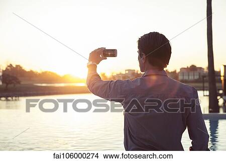 Picture - Man photographing sunset with smartphone. Fotosearch