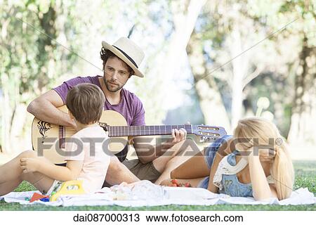 Stock Image - Man playing acoustic guitar for wife and son. Fotosearch