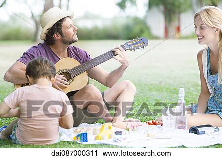 Stock Image - Man playing acoustic guitar next to wife and son. Fotosearch