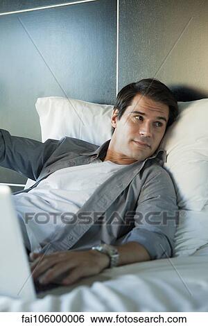 Man relaxing in bed with laptop computer View Large Photo Image Stock Photograph - Man relaxing in bed with laptop computer. Fotosearch