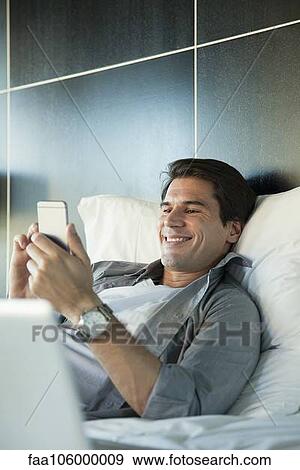 Man relaxing in bed with multimedia smartphone View Large Photo Image Stock Photo - Man relaxing in bed with multimedia smartphone. Fotosearch