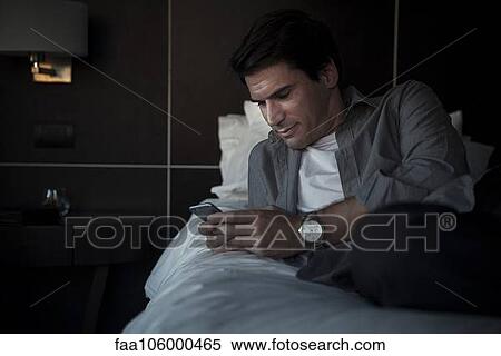 Man relaxing on bed with multimedia smartphone View Large Photo Image Stock Photography - Man relaxing on bed with multimedia smartphone. Fotosearch