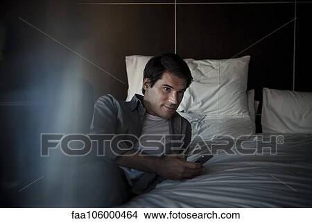 Man relaxing on bed with smartphone View Large Photo Image Picture - Man relaxing on bed with smartphone. Fotosearch