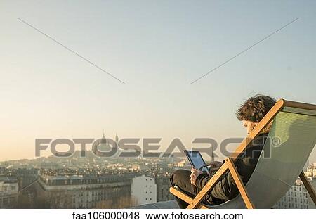Man relaxing on rooftop terrace with digital tablet View Large Photo Image Stock Photo - Man relaxing on rooftop terrace with digital tablet. Fotosearch