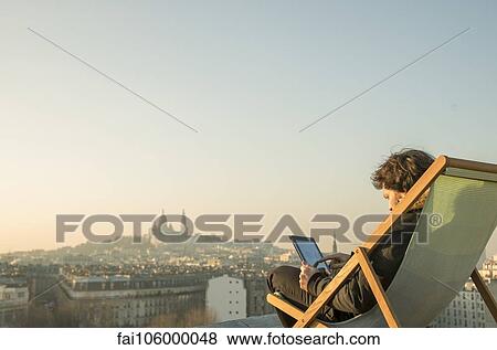 Man relaxing on rooftop terrace with digital tablet View Large Photo Image Stock Photo - Man relaxing on rooftop terrace with digital tablet. Fotosearch
