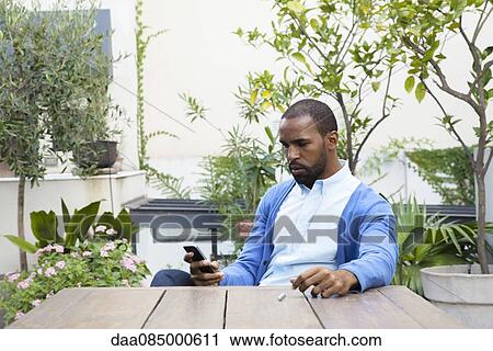 Man seated at table in courtyard making phone call View Large Photo Image Stock Image - Man seated at table in courtyard making phone call. Fotosearch