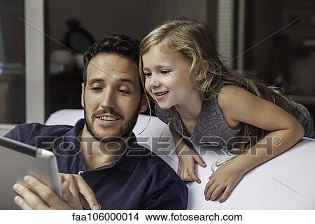 Picture - Man showing daughter video streaming on digital tablet. Fotosearch