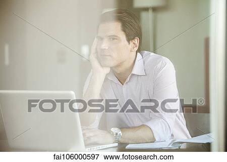 Stock Photo - Man sitting before laptop computer, daydreaming in office. Fotosearch