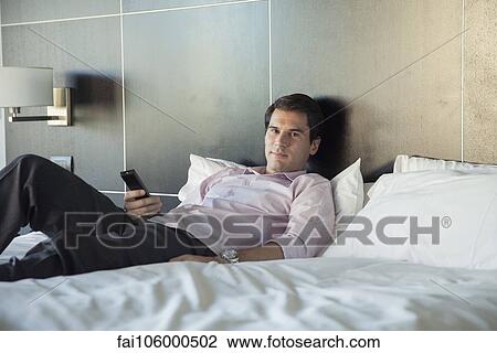 Man unwinding after work by watching TV on bed View Large Photo Image Stock Image - Man unwinding after work by watching TV on bed. Fotosearch