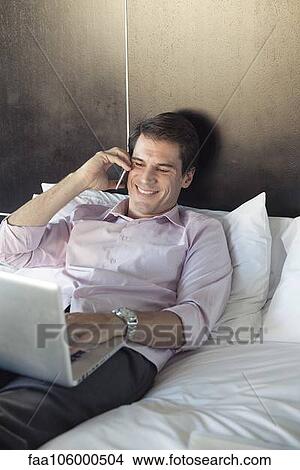 Man using laptop computer and cell phone in bed View Large Photo Image Picture - Man using laptop computer and cell phone in bed. Fotosearch