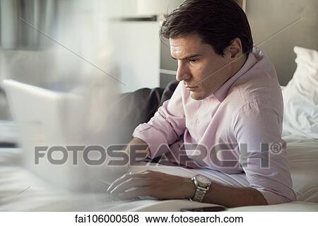 Man using laptop computer on bed View Large Photo Image Stock Photo - Man using laptop computer on bed. Fotosearch