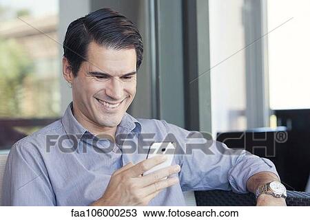Stock Image - Man using smartphone and smiling cheerfully. Fotosearch
