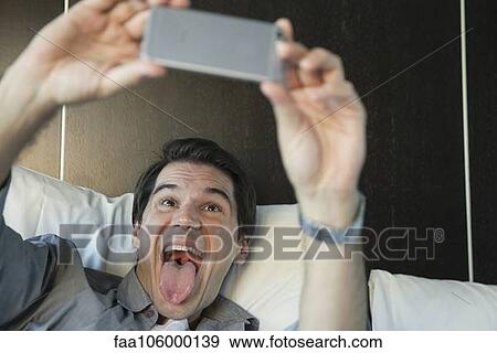 Man using smartphone to take a selfie, sticking out tongue View Large Photo Image Stock Photo - Man using smartphone to take a selfie, sticking out tongue. Fotosearch