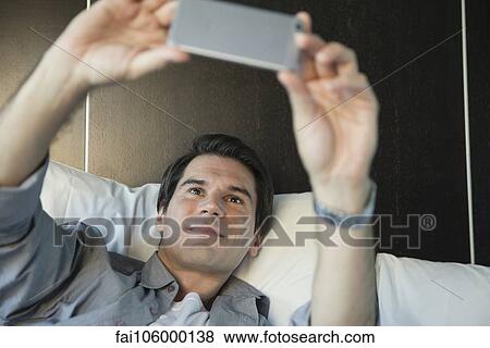 Stock Photo - Man using smartphone to take a selfie. Fotosearch