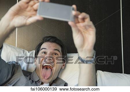 Man using smartphone to take a selfie, sticking out tongue View Large Photo Image Stock Photo - Man using smartphone to take a selfie, sticking out tongue. Fotosearch