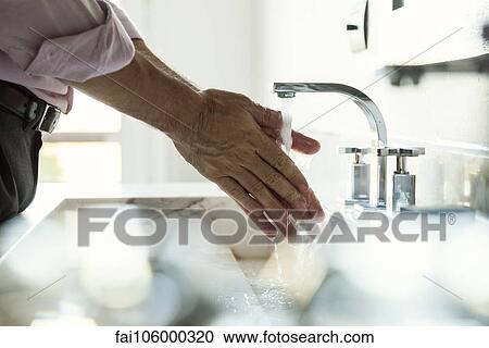 Stock Image - Man washing hands in bathroom sink, cropped. Fotosearch