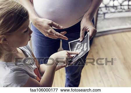 Mother using ultrasound photo to prepare daughter for imminent arrival of new sibling View Large Photo Image Stock Photo - Mother using ultrasound photo to prepare daughter for imminent arrival of new sibling. Fotosearch