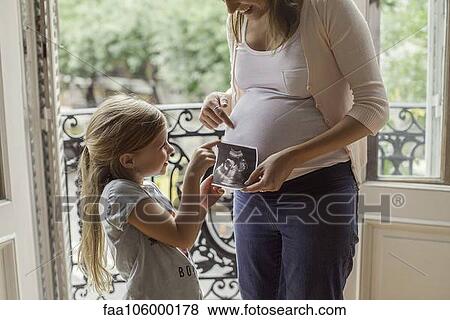 Stock Photo - Mother using ultrasound photo to prepare daughter for imminent arrival of new sibling. Fotosearch