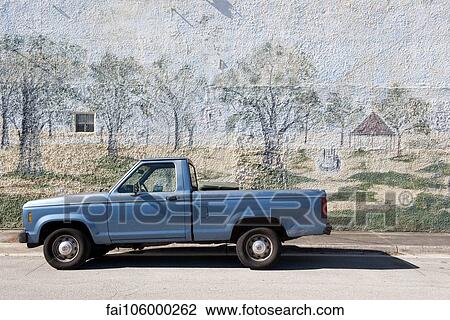 Stock Image - Pick-up truck parked beside wall with mural painted on it. Fotosearch