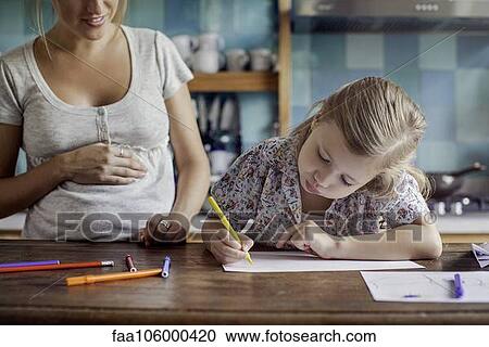Stock Image - Pregnant mother looking on as daughter draws. Fotosearch