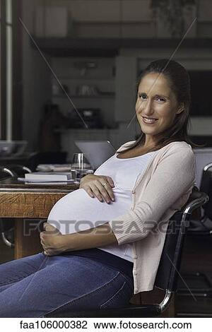 Stock Image - Pregnant woman cradling belly, portrait. Fotosearch