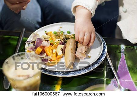 Stock Photo - Toddler eating sausage with hands. Fotosearch