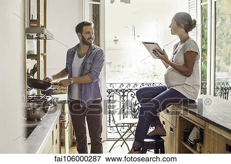 Stock Photo - Wife looking on as husband prepares meal. Fotosearch