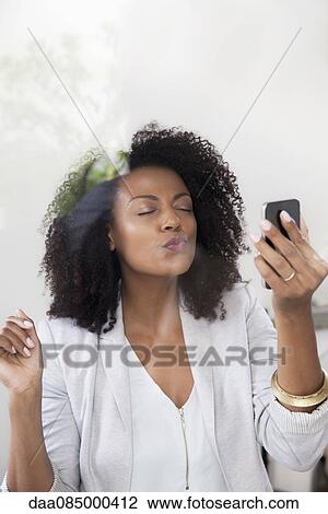 Woman blowing kiss at smartphone while doing video chat View Large Photo Image Stock Image - Woman blowing kiss at smartphone while doing video chat. Fotosearch