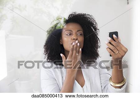 Stock Image - Woman blowing kiss at smartphone while doing video chat. Fotosearch