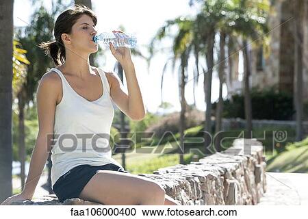 Stock Image - Woman drinking bottled water in park. Fotosearch
