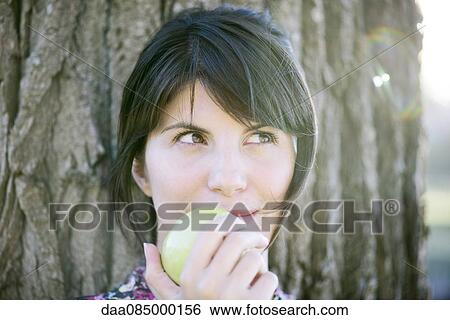 Stock Photograph - Woman eating apple, looking up thoughtfully. Fotosearch