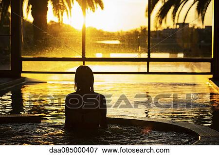 Stock Photo - Woman in indoor pool during sunset. Fotosearch