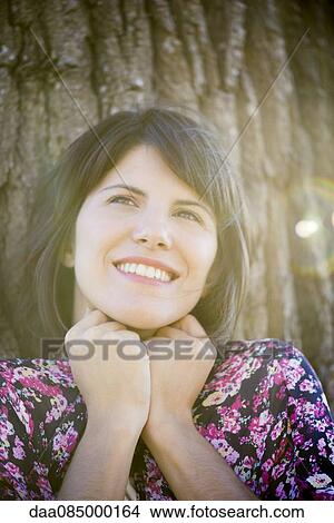 Picture - Woman leaning against tree, smiling, portrait. Fotosearch