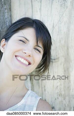 Woman leaning against tree trunk, smilling cheerfully, portrait View Large Photo Image Picture - Woman leaning against tree trunk, smilling cheerfully, portrait. Fotosearch