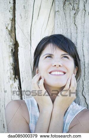 Woman leaning against tree trunk, looking up and smiling hopefully View Large Photo Image Stock Photo - Woman leaning against tree trunk, looking up and smiling hopefully. Fotosearch