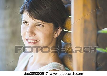 Stock Photo - Woman leaning against wall, smiling, portrait. Fotosearch
