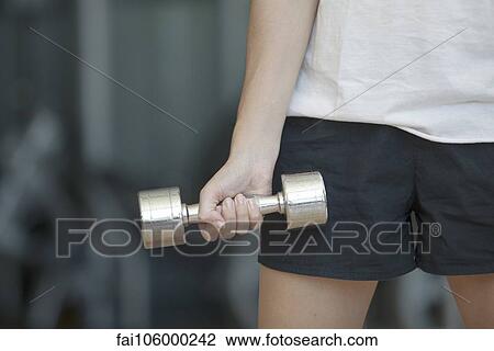 Stock Image - Woman lifting dumbbell, cropped. Fotosearch