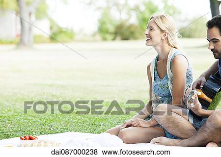 Woman listening to man playing acoustic guitar while picnicking in park View Large Photo Image Stock Photo - Woman listening to man playing acoustic guitar while picnicking in park. Fotosearch