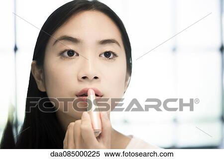 Stock Photography - Woman looking in mirror, applying lipstick. Fotosearch