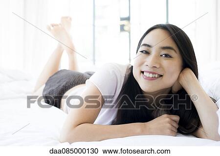 Woman lying on bed, smiling cheerfully View Large Photo Image Stock Image - Woman lying on bed, smiling cheerfully. Fotosearch