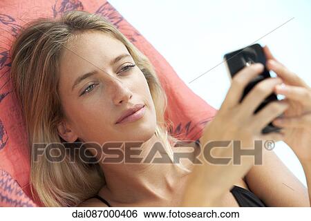Stock Photograph - Woman relaxing on lounge chair using smartphone. Fotosearch