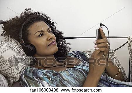 Woman relaxing to tunes playing on smartphone View Large Photo Image Stock Photo - Woman relaxing to tunes playing on smartphone. Fotosearch