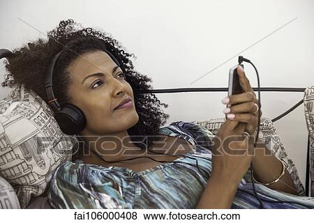 Woman relaxing to tunes playing on smartphone View Large Photo Image Stock Photo - Woman relaxing to tunes playing on smartphone. Fotosearch