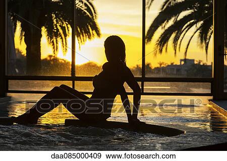 Stock Photo - Woman resting at edge of pool during sunset. Fotosearch