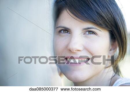 Stock Photo - Woman resting head on tree trunk, smiling cheerfully. Fotosearch