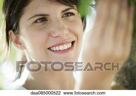 Stock Image - Woman touching tree, smiling, portrait. Fotosearch