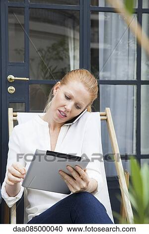 Woman using digital tablet while making phone call View Large Photo Image Stock Image - Woman using digital tablet while making phone call. Fotosearch