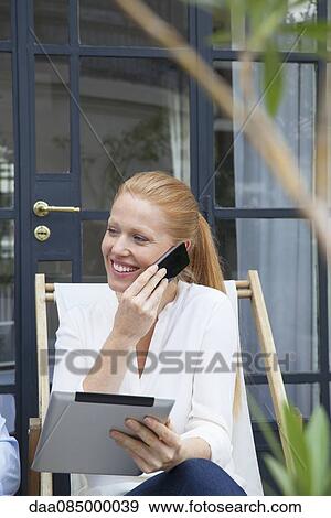 Woman using digital tablet while talking on cell phone View Large Photo Image Stock Photo - Woman using digital tablet while talking on cell phone. Fotosearch