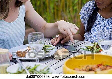 Women looking at smartphone while dining together outdoors View Large Photo Image Stock Photo - Women looking at smartphone while dining together outdoors. Fotosearch