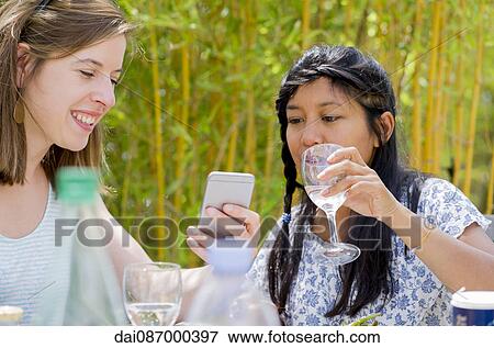 Women relaxing together outdoors, looking at smartphone View Large Photo Image Stock Photo - Women relaxing together outdoors, looking at smartphone. Fotosearch